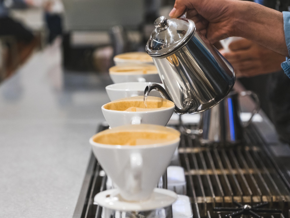 A barista brews several V60s in a coffee shop.