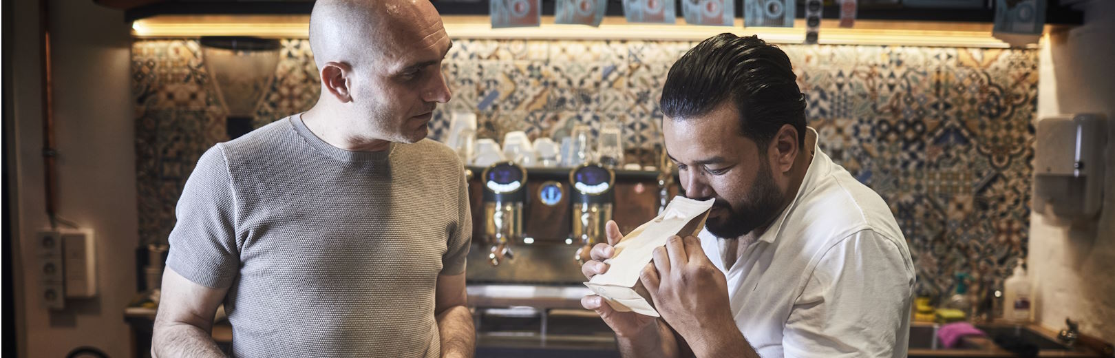 Two men assess aroma of a roasted bag of coffee.