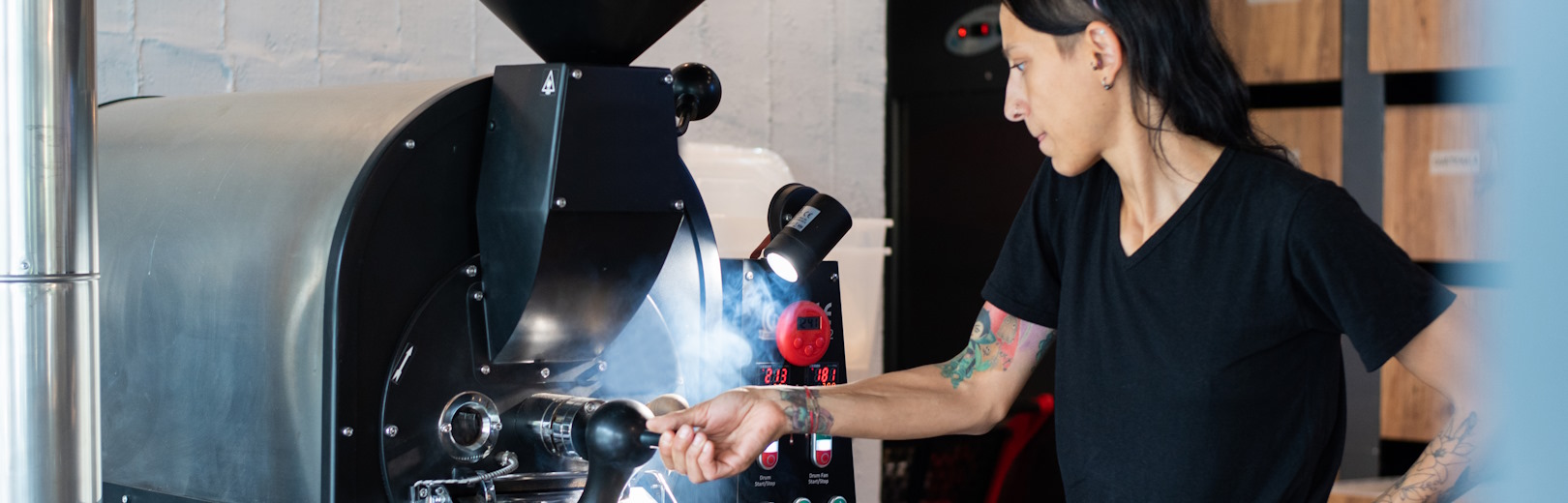 A woman unloads roasted coffee from a roasting machine.