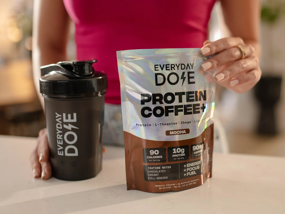 A person scoops Everyday Dose Protein Coffee into a protein shaker.